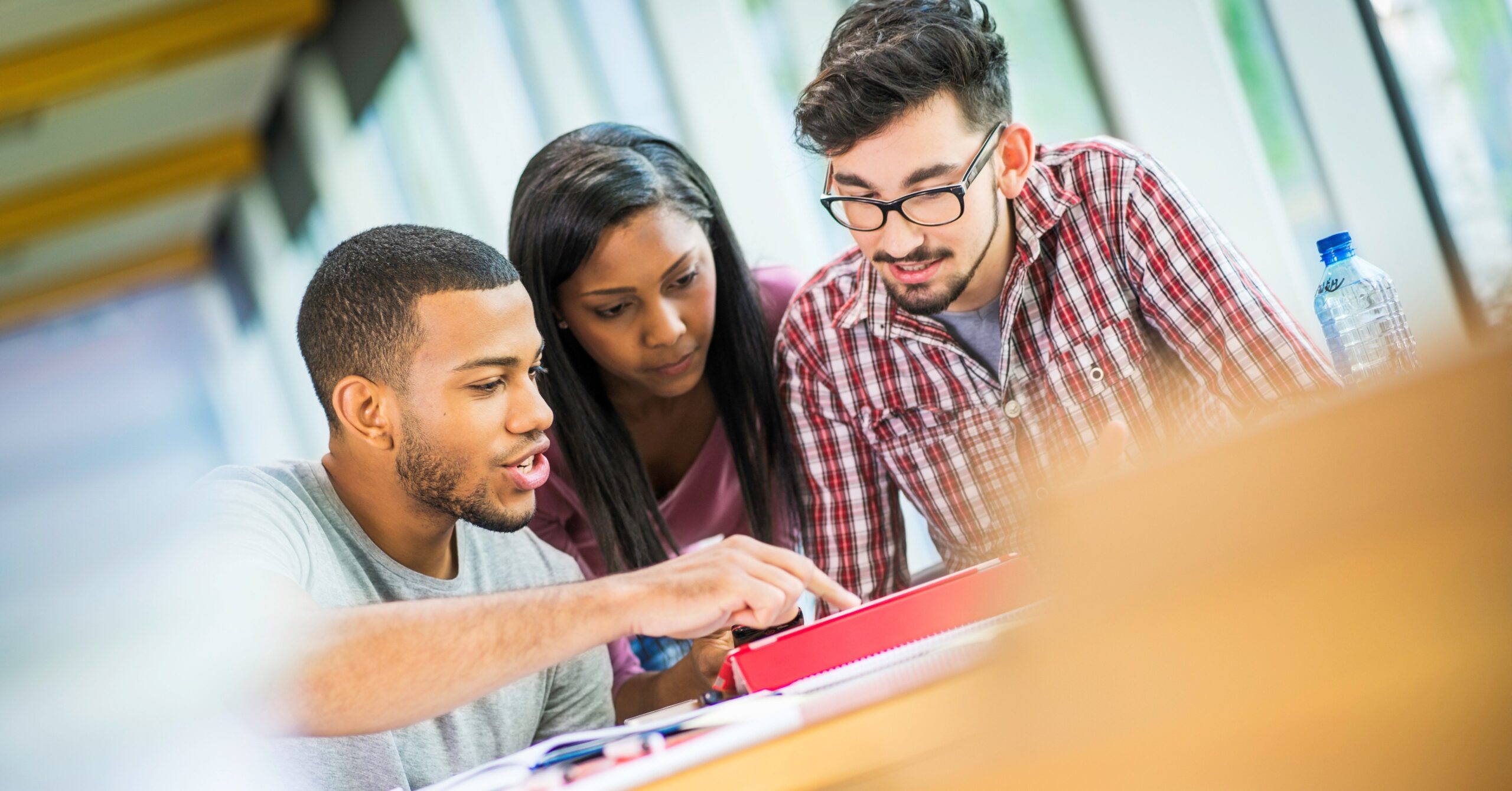 A group of students sit at a table and look at a laptop.