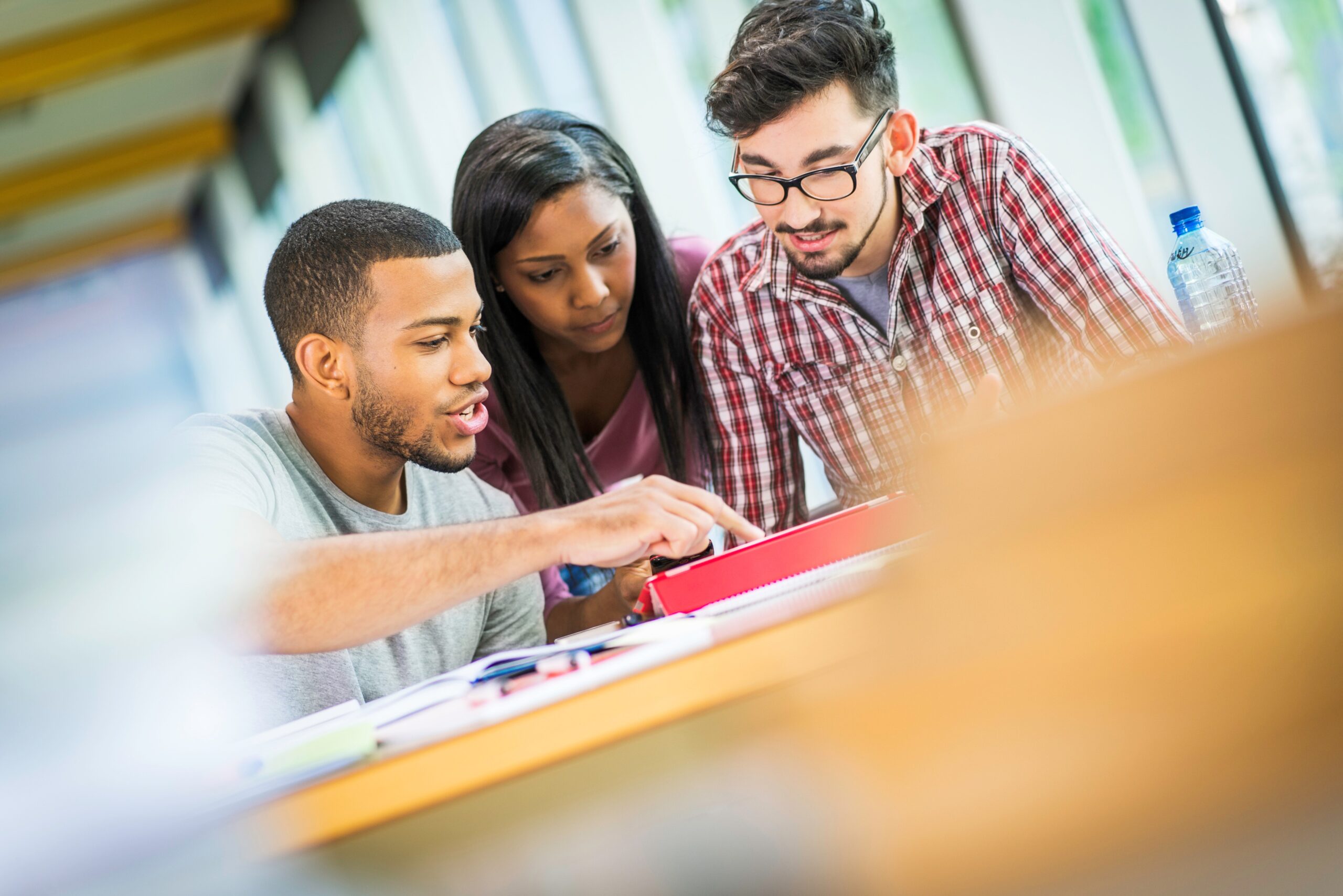 A group of students sit at a table and look at a laptop.